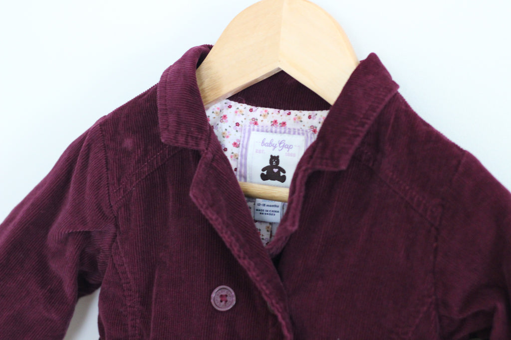 A burgundy corduroy baby jacket hanging on a wooden hanger against a plain white background. The jacket features a pointed collar, a button closure, and a visible 'baby Gogo' brand label.