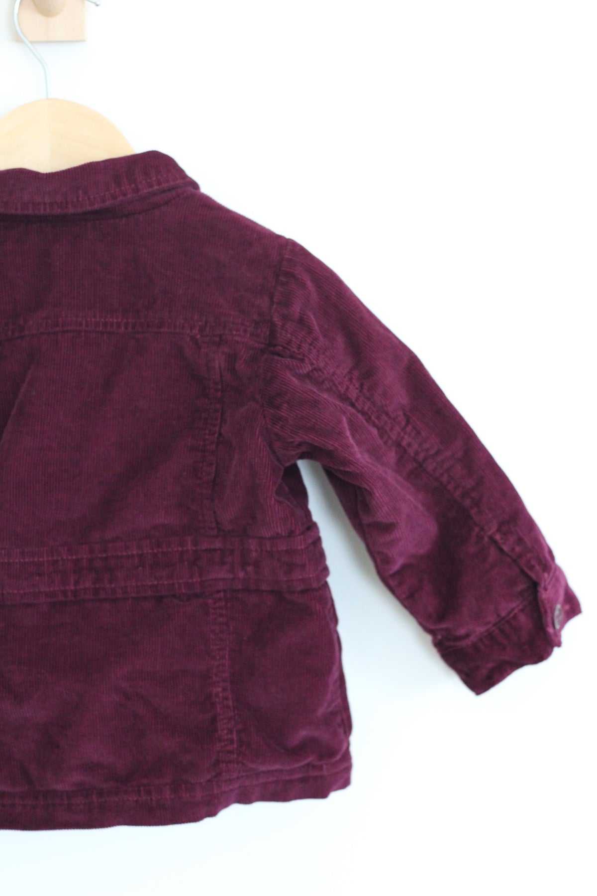 A burgundy corduroy jacket hanging on a wooden hanger against a plain white background.