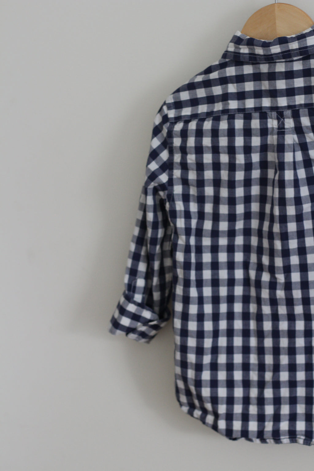 A navy and white gingham check long-sleeve shirt hanging on a wooden hanger against a plain light gray wall.
