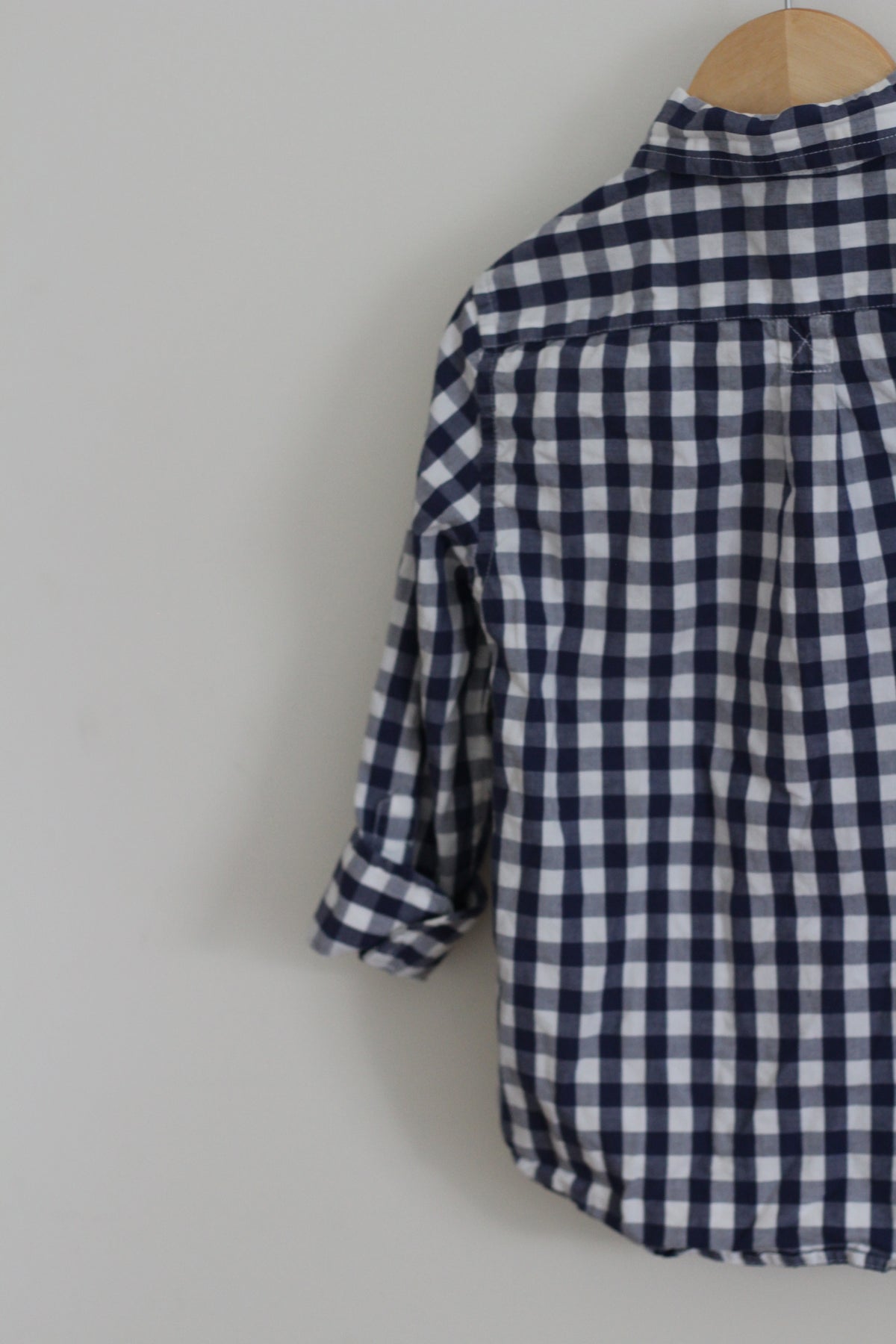 A navy and white gingham check long-sleeve shirt hanging on a wooden hanger against a plain light gray wall.
