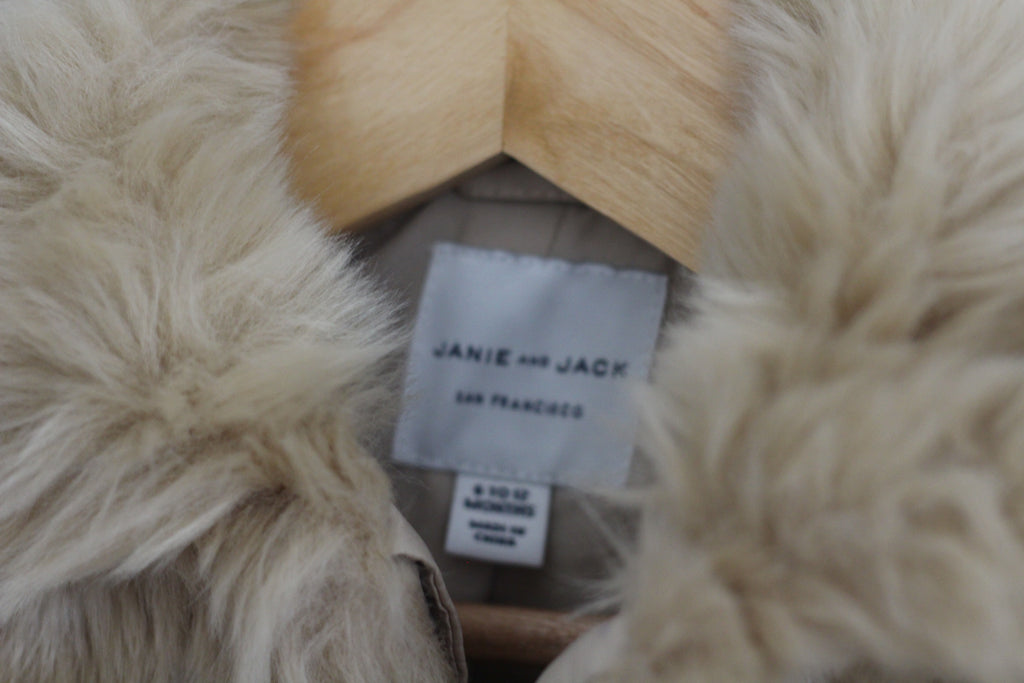 Close-up of a fluffy cream-colored faux fur garment with a visible white fabric label reading 'JANIE AND JACK' and 'SAN FRANCISCO'.