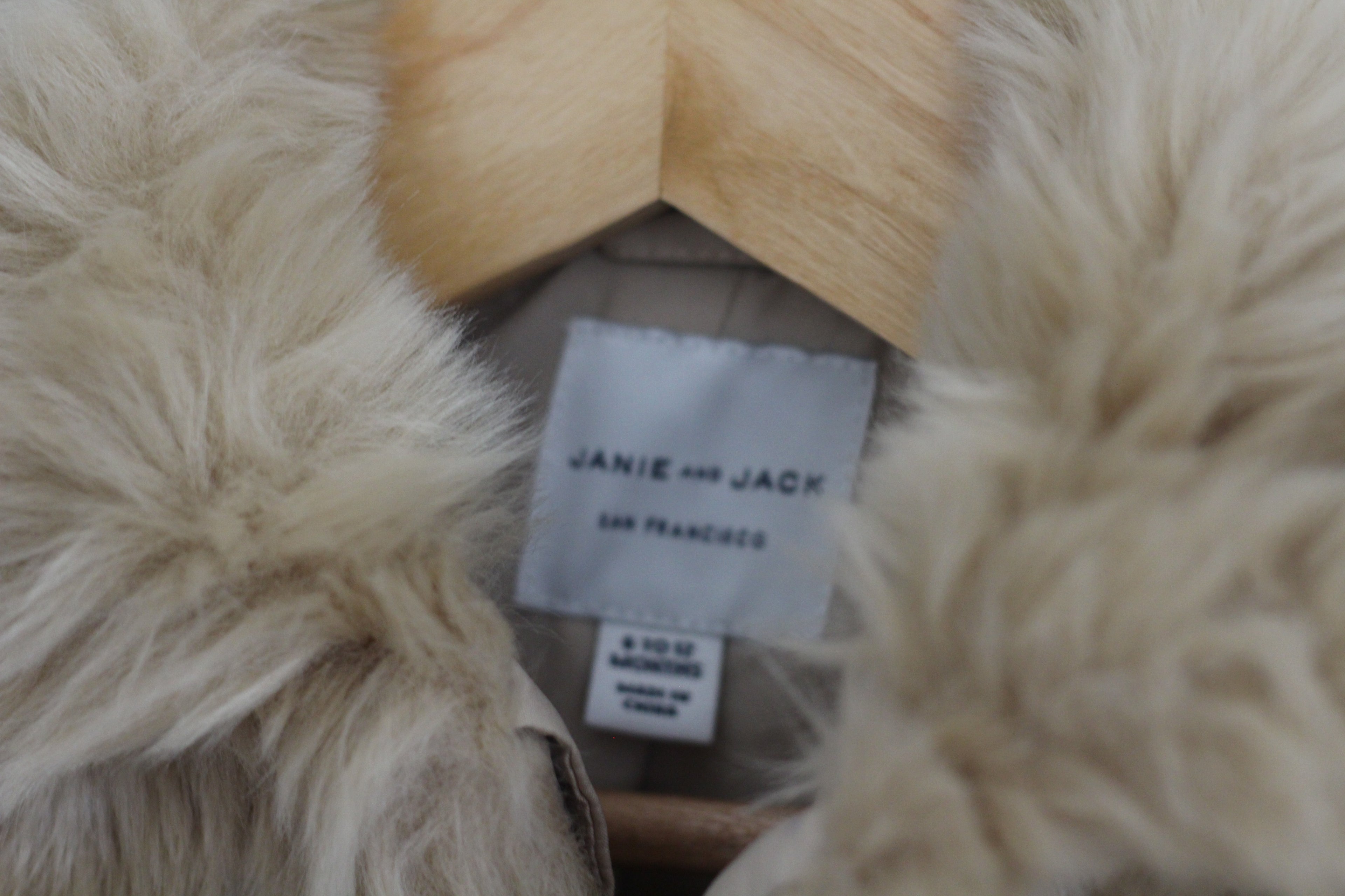 Close-up of a fluffy cream-colored faux fur garment with a visible white fabric label reading 'JANIE AND JACK' and 'SAN FRANCISCO'.